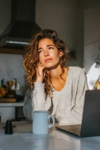 Woman looking thoughtful with coffee and laptop, symbolizing concerns about Ryze Mushroom Coffee on Amazon