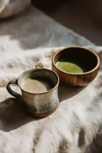 Ceramic cup of mushroom coffee beside a bowl of vibrant green matcha on a linen cloth